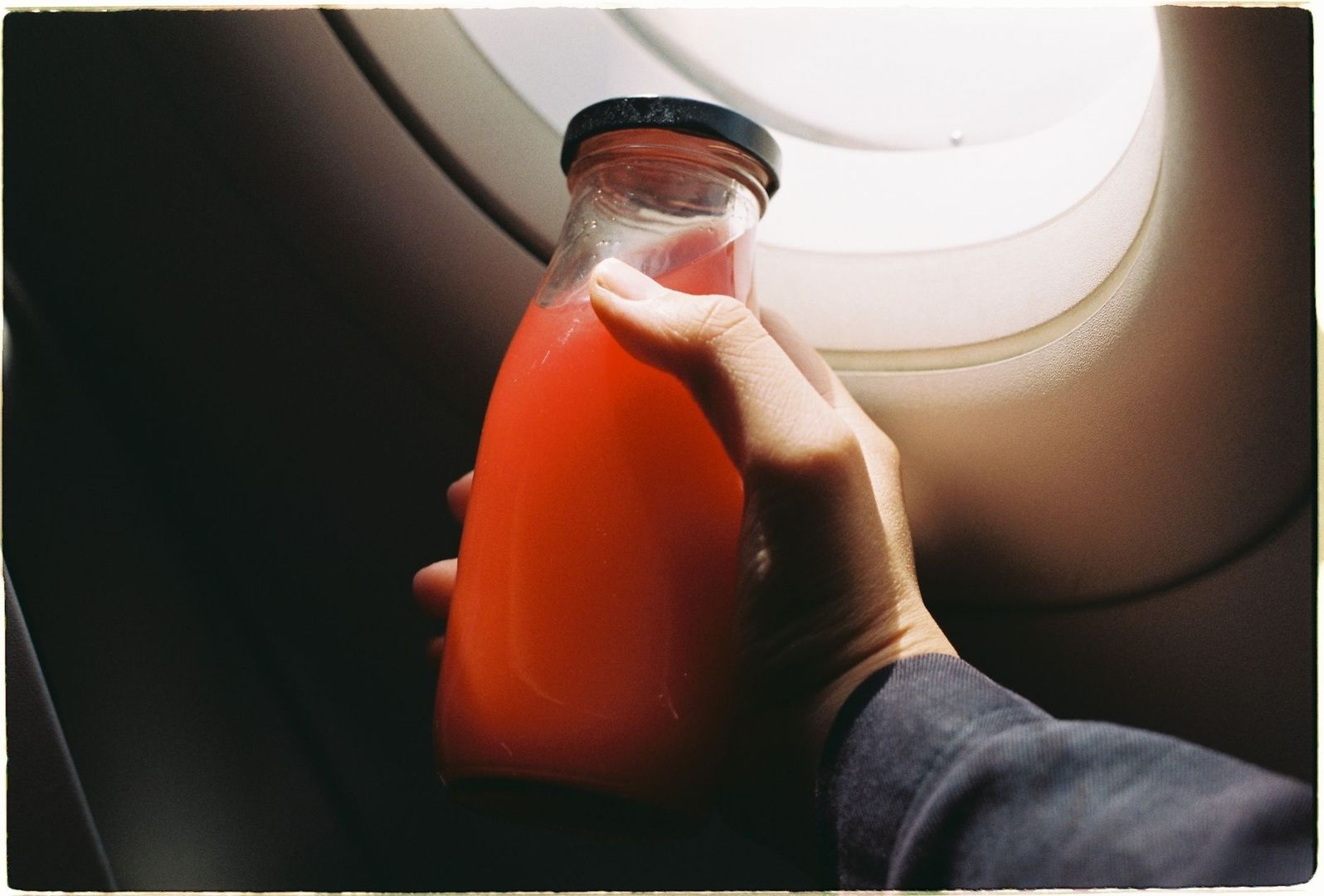 Hånd holder en flaske tomatjuice ved et flyvindu