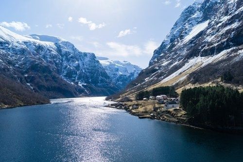 Snødekte fjell og en fjord med en liten bosetning langs bredden